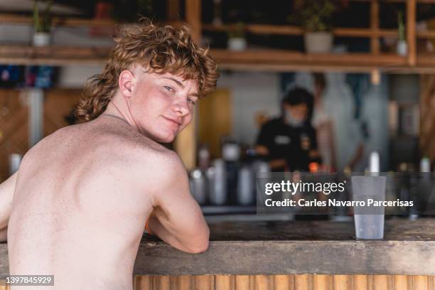 man with a retro hairstyle sitting at a beach bar turning to look at the camera - wavy hair beach stock pictures, royalty-free photos & images