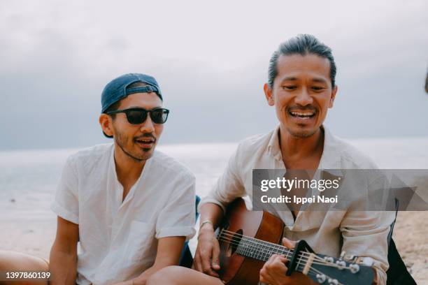 two men playing guitar and singing on beach - male friends hanging out ストックフォトと画像