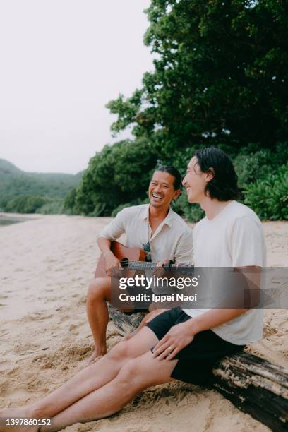 men playing guitar and singing on beach at dusk - アウトドア　日本人 ストックフォトと画像