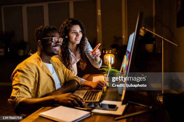 joven ingeniera de ti señalando datos en la pantalla de la computadora mientras discute el punto de trabajo con un colega africano - female exhibitionist fotografías e imágenes de stock
