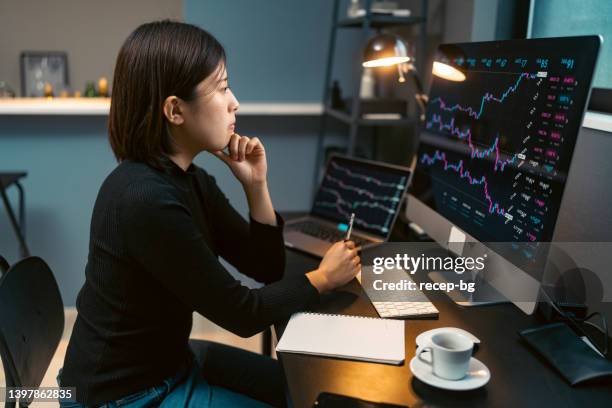 young woman doing cryptocurrency business trading on her computer at home at nigh - valores imagens e fotografias de stock