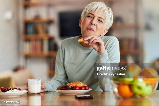 smiling senior woman eating breakfast at home. - mature women eating stock pictures, royalty-free photos & images