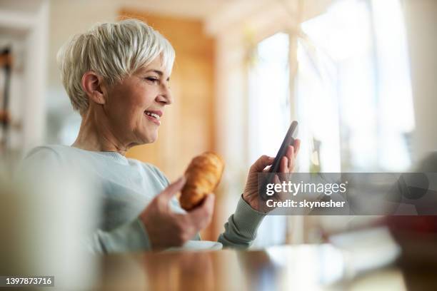 happy senior woman using cell phone during breakfast at home. - franse gerechten stockfoto's en -beelden