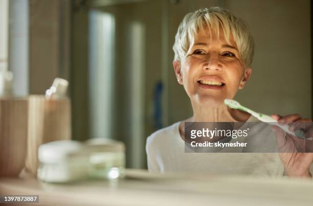 reflection in a mirror of happy mature woman brushing her teeth. - brushing teeth stock pictures, royalty-free photos & images