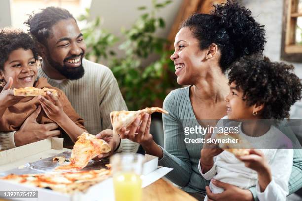 famiglia nera felice che parla mentre mangia la pizza per il pranzo in sala da pranzo. - african family eating foto e immagini stock