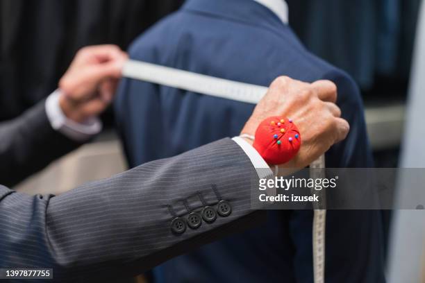 male tailor with pin cushion measuring customer's shoulders - tailor suit stock pictures, royalty-free photos & images