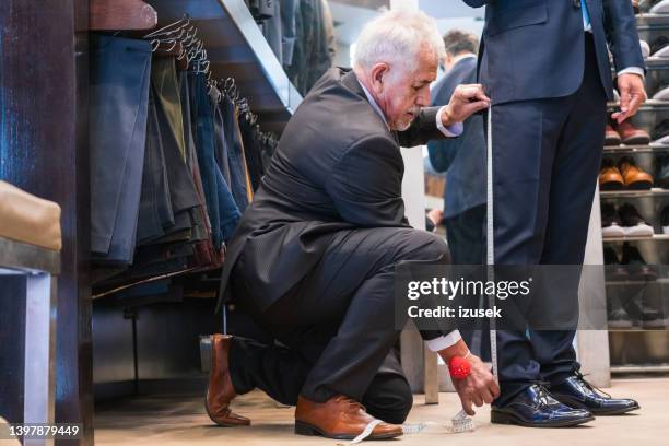 leitender männlicher schneider, der die hosenlänge des kunden misst - trousers stock-fotos und bilder