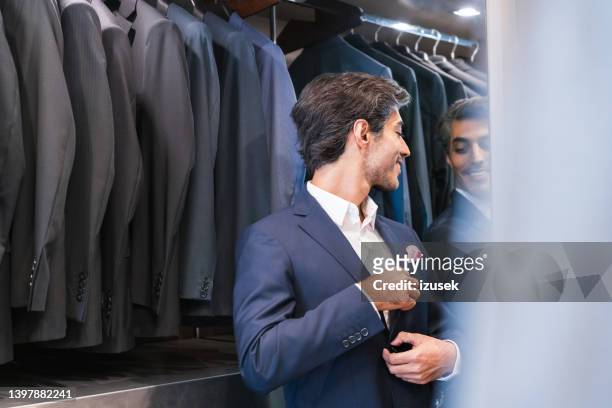 uomo sorridente che prova l'abito che guarda il riflesso sullo specchio - man reflection foto e immagini stock