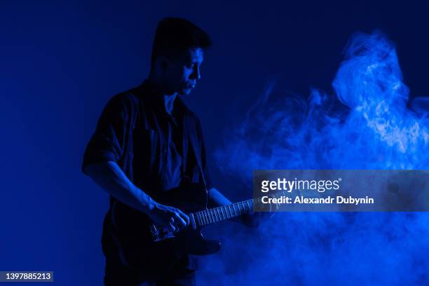 silhouette of a male guitarist playing guitar music in blue neon light in smoke with copy space. - concert face stock pictures, royalty-free photos & images