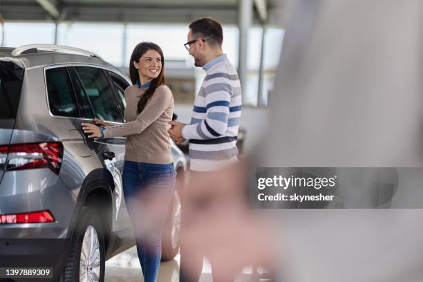happy couple talking while buying a new car in a showroom. - car owner stock pictures, royalty-free photos & images