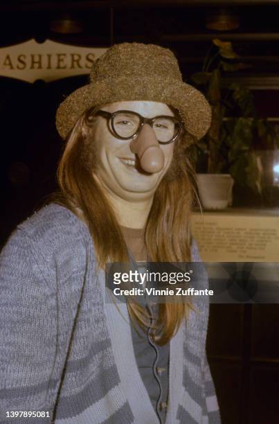British singer and songwriter Ozzy Osbourne, wearing a blue striped cardigan with a brown hat and a pair of 'nose glasses' which feature a penis over...