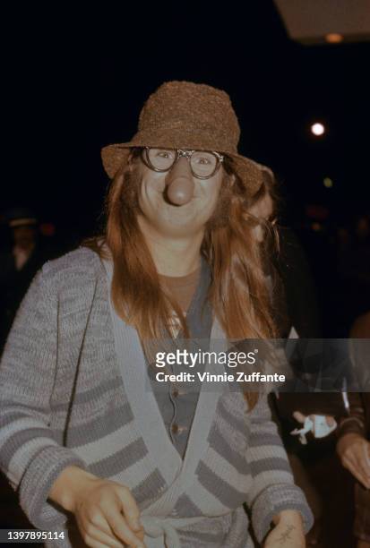 British singer and songwriter Ozzy Osbourne, wearing a blue striped cardigan with a brown hat and a pair of 'nose glasses' which feature a penis over...