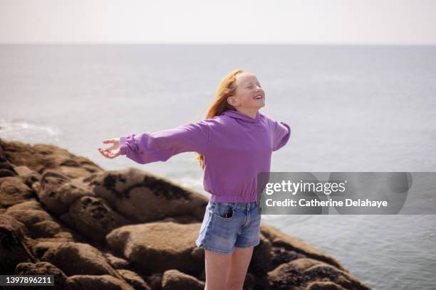 portrait of a smiling young girl facing the wind standing on the rock - young teen girl beach ストックフォトと画像