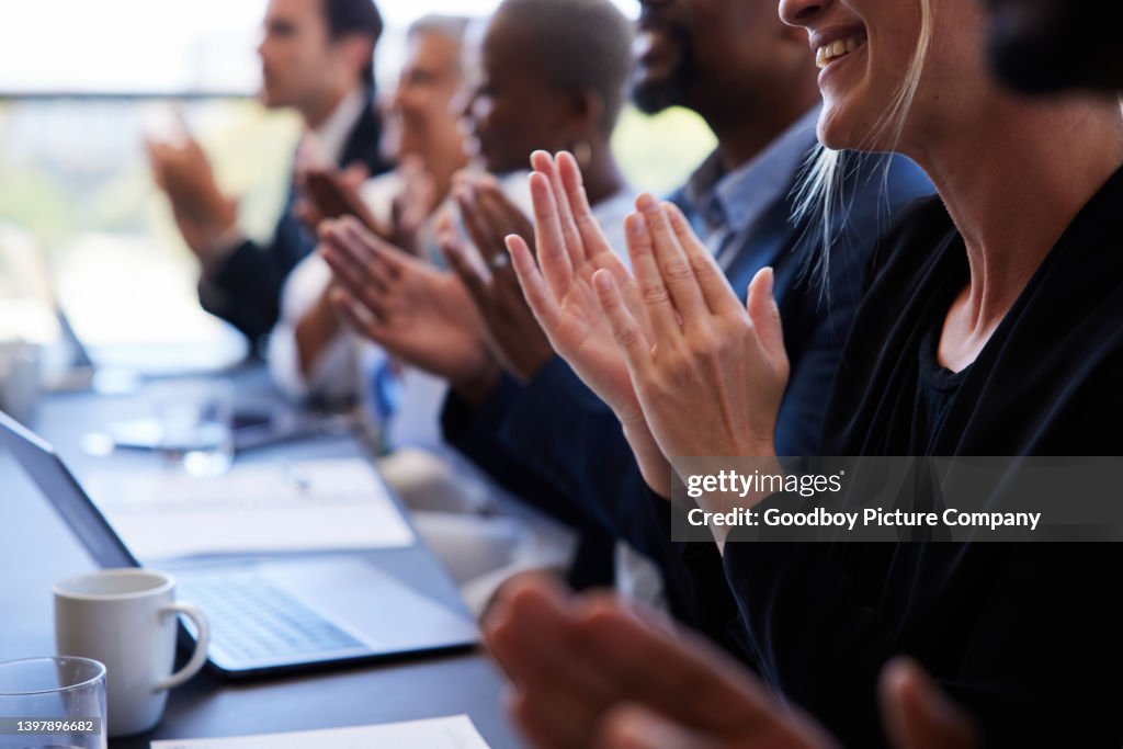 Diversi uomini d'affari seduti insieme a un tavolo della sala riunioni e applaudendo