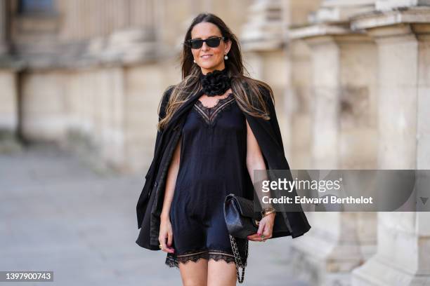 Alba Garavito Torre wears black sunglasses from Ray Ban, a white pearl earrings, a black oversized flower ribbon necklace, a black lace V-neck silk...