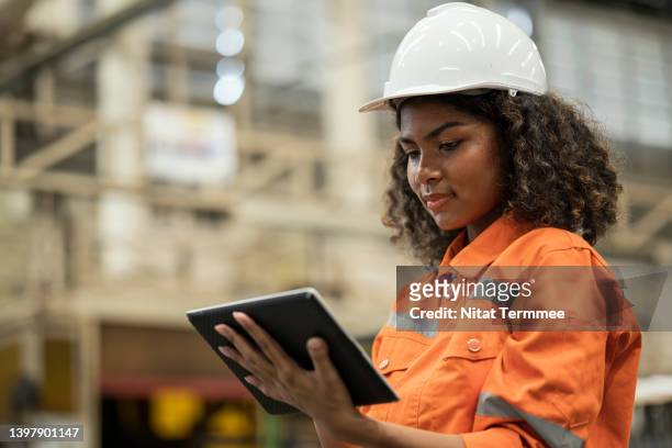 shop floor control to managing operations in real-time. african american production control engineer holding a tablet and standing in production line while using software tool to audit production progress and the amount of raw materials used. - african ethnicity stock photos et images de collection