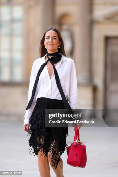 Alba Garavito Torre wears white pearl earrings, a white V-neck shirt, a black ribbon with embroidered flower necklace, a red shiny grained leather...