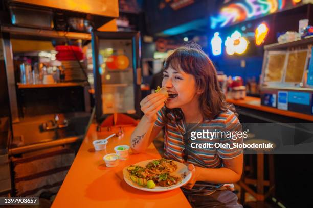 mujer comiendo taco en un bar - taco fotografías e imágenes de stock