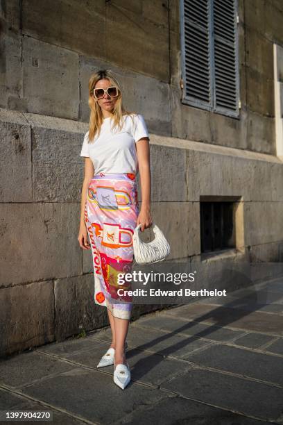 Natalia Verza wears white sunglasses from Louis Vuitton, a white t-shirt, a multicolored silk print pattern scarf as a midi skirt from Louis Vuitton,...