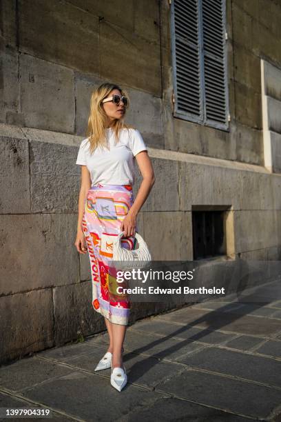 Natalia Verza wears white sunglasses from Louis Vuitton, a white t-shirt, a multicolored silk print pattern scarf as a midi skirt from Louis Vuitton,...