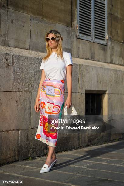 Natalia Verza wears white sunglasses from Louis Vuitton, a white t-shirt, a multicolored silk print pattern scarf as a midi skirt from Louis Vuitton,...