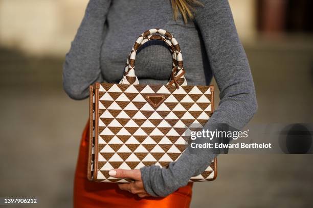 Natalia Verza wears a gray turtleneck wool pullover, an orange silk knees tube skirt from Prada, a brown and white triangular print pattern handbag...