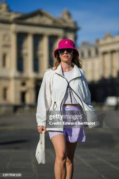 Maria Rosaria Rizzo wears a pink fuchsia bob hat from Kangol, gray sunglasses, silver earrings, a white t-shirt, a white zipper rain coat, pale...