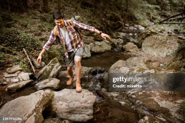 young casually clothed hiker crossing small river - stepping stone stock pictures, royalty-free photos & images