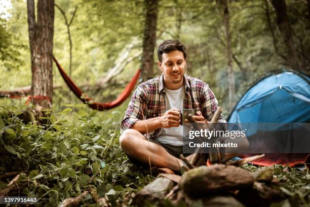 young casually clothed hiker drinking tea near the campfire - hysa bildbanksfoton och bilder