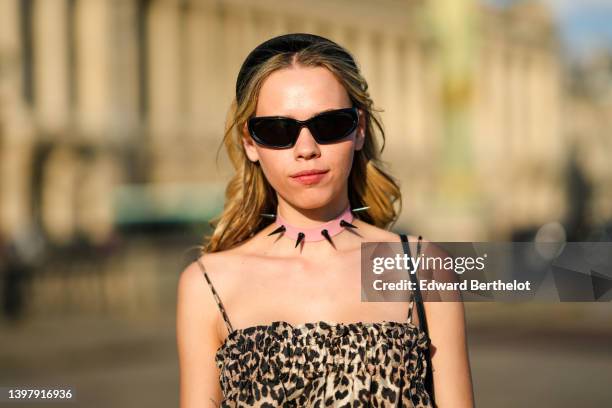 Almuneda Lapique wears black sunglasses, a pink shiny leather with large black studs necklace, a beige and black leopard print pattern tank-top /...