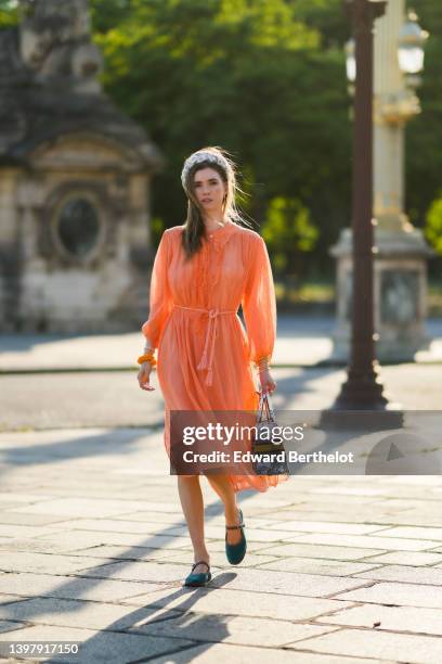 Zita d'Hauteville wears a white latte with blue embroidered flower pattern / braided silk headband, gold earrings, an orange ruffled / ribbed / long...