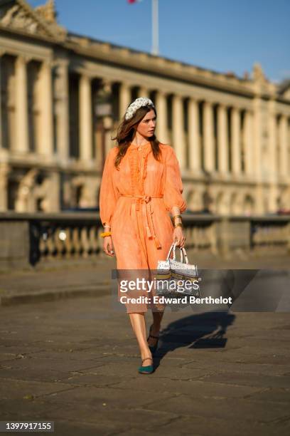 Zita d'Hauteville wears a white latte with blue embroidered flower pattern / braided silk headband, gold earrings, an orange ruffled / ribbed / long...