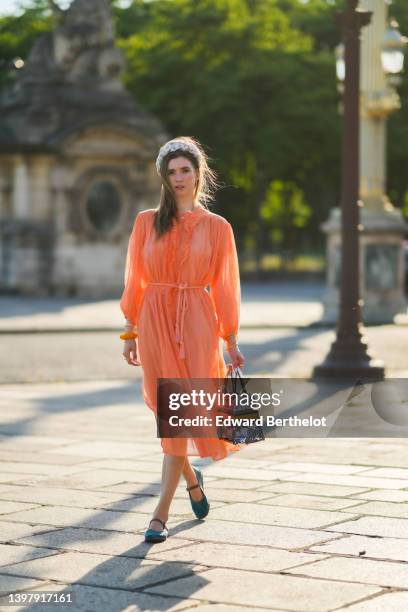 Zita d'Hauteville wears a white latte with blue embroidered flower pattern / braided silk headband, gold earrings, an orange ruffled / ribbed / long...