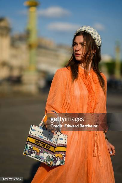 Zita d'Hauteville wears a white latte with blue embroidered flower pattern / braided silk headband, gold earrings, an orange ruffled / ribbed / long...