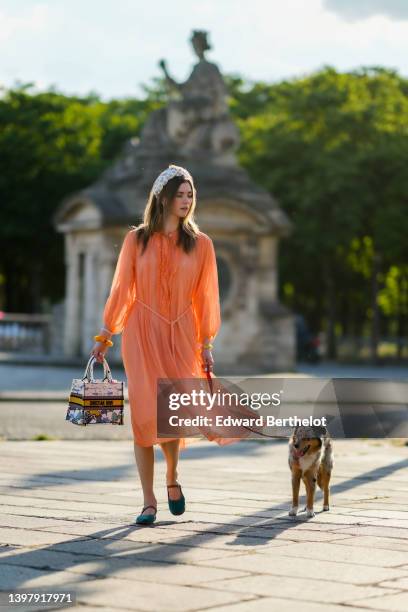 Zita d'Hauteville wears a white latte with blue embroidered flower pattern / braided silk headband, gold earrings, an orange ruffled / ribbed / long...