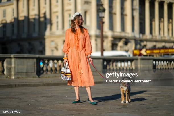 Zita d'Hauteville wears a white latte with blue embroidered flower pattern / braided silk headband, gold earrings, an orange ruffled / ribbed / long...