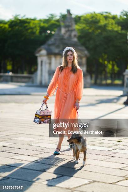 Zita d'Hauteville wears a white latte with blue embroidered flower pattern / braided silk headband, gold earrings, an orange ruffled / ribbed / long...