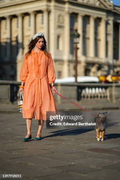 Zita d'Hauteville wears a white latte with blue embroidered flower pattern / braided silk headband, gold earrings, an orange ruffled / ribbed / long...