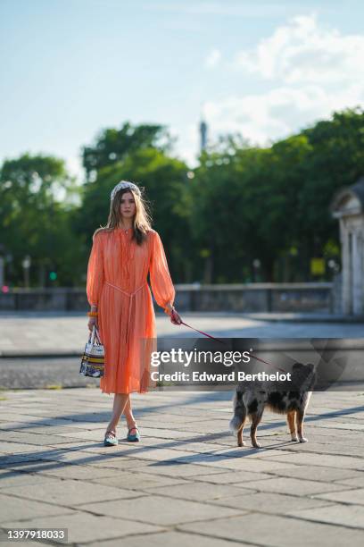 Zita d'Hauteville wears a white latte with blue embroidered flower pattern / braided silk headband, gold earrings, an orange ruffled / ribbed / long...