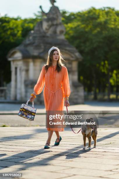 Zita d'Hauteville wears a white latte with blue embroidered flower pattern / braided silk headband, gold earrings, an orange ruffled / ribbed / long...