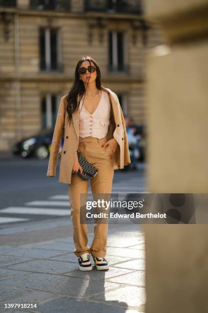 Gabriella Berdugo wears brown sunglasses, a white denim V-neck / buttoned / sleeveless gilet, a beige denim with pale pink embroidered flower...