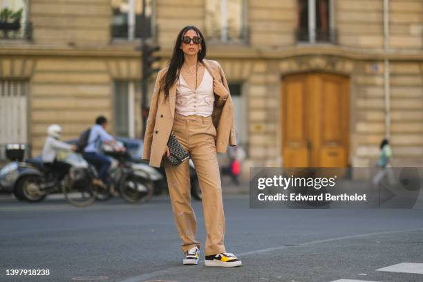 Gabriella Berdugo wears brown sunglasses, a white denim V-neck / buttoned / sleeveless gilet, a beige denim with pale pink embroidered flower...