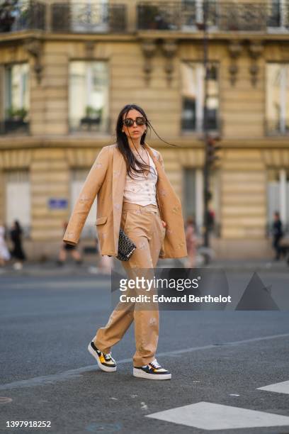 Gabriella Berdugo wears brown sunglasses, a white denim V-neck / buttoned / sleeveless gilet, a beige denim with pale pink embroidered flower...