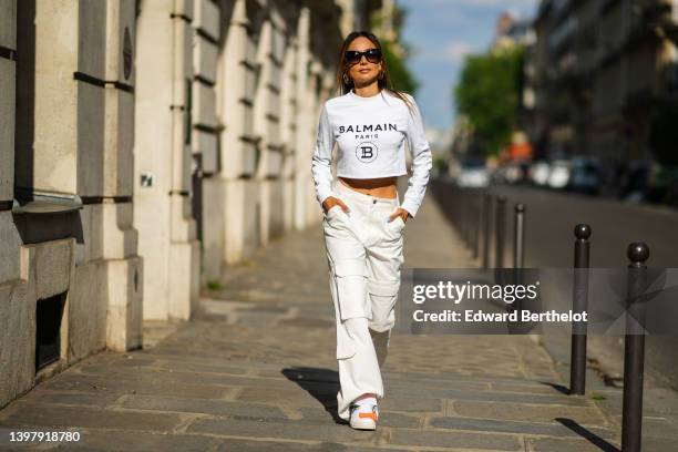 Patricia Gloria Contreras wears black oversized sunglasses, a gold logo earrings from Louis Vuitton, a white long sleeves / with black logo print...