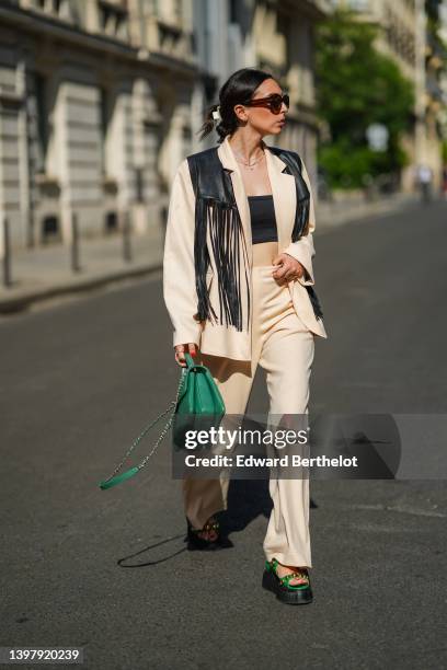 Gabriella Berdugo wears a white hair clip, black sunglasses, gold and silver pendant necklaces, a black shoulder-off / cropped top, a black shiny...