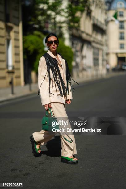 Gabriella Berdugo wears a white hair clip, black sunglasses, gold and silver pendant necklaces, a black shoulder-off / cropped top, a black shiny...