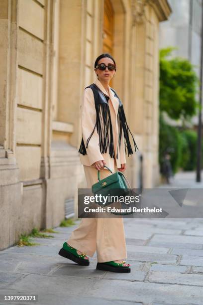 Gabriella Berdugo wears a white hair clip, black sunglasses, gold and silver pendant necklaces, a black shoulder-off / cropped top, a black shiny...