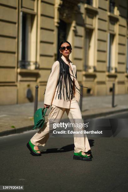 Gabriella Berdugo wears a white hair clip, black sunglasses, gold and silver pendant necklaces, a black shoulder-off / cropped top, a black shiny...