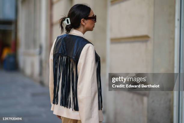 Gabriella Berdugo wears a white hair clip, black sunglasses, gold and silver pendant necklaces, a black shoulder-off / cropped top, a black shiny...