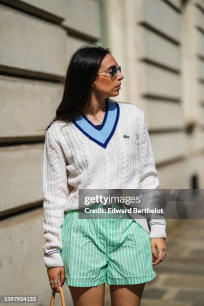 Gabriella Berdugo wears blue sunglasses, gold pendant earrings, a gold chain pendant necklace, a navy blue t-shirt, a white latte braided wool...